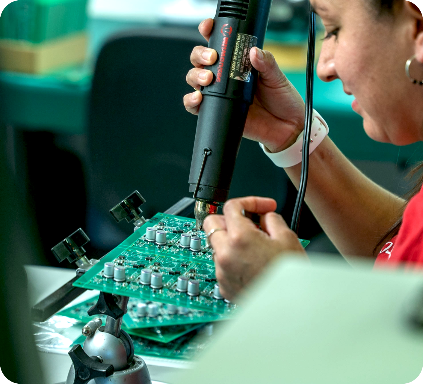 A person is using a hot air tool to work on a green printed circuit board.